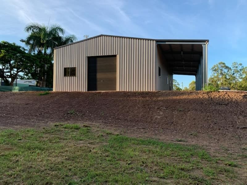 A Large Shed With A Garage Door Is Sitting On Top Of A Dirt Hill — Bushman Sheds in Bundaberg East, QLD