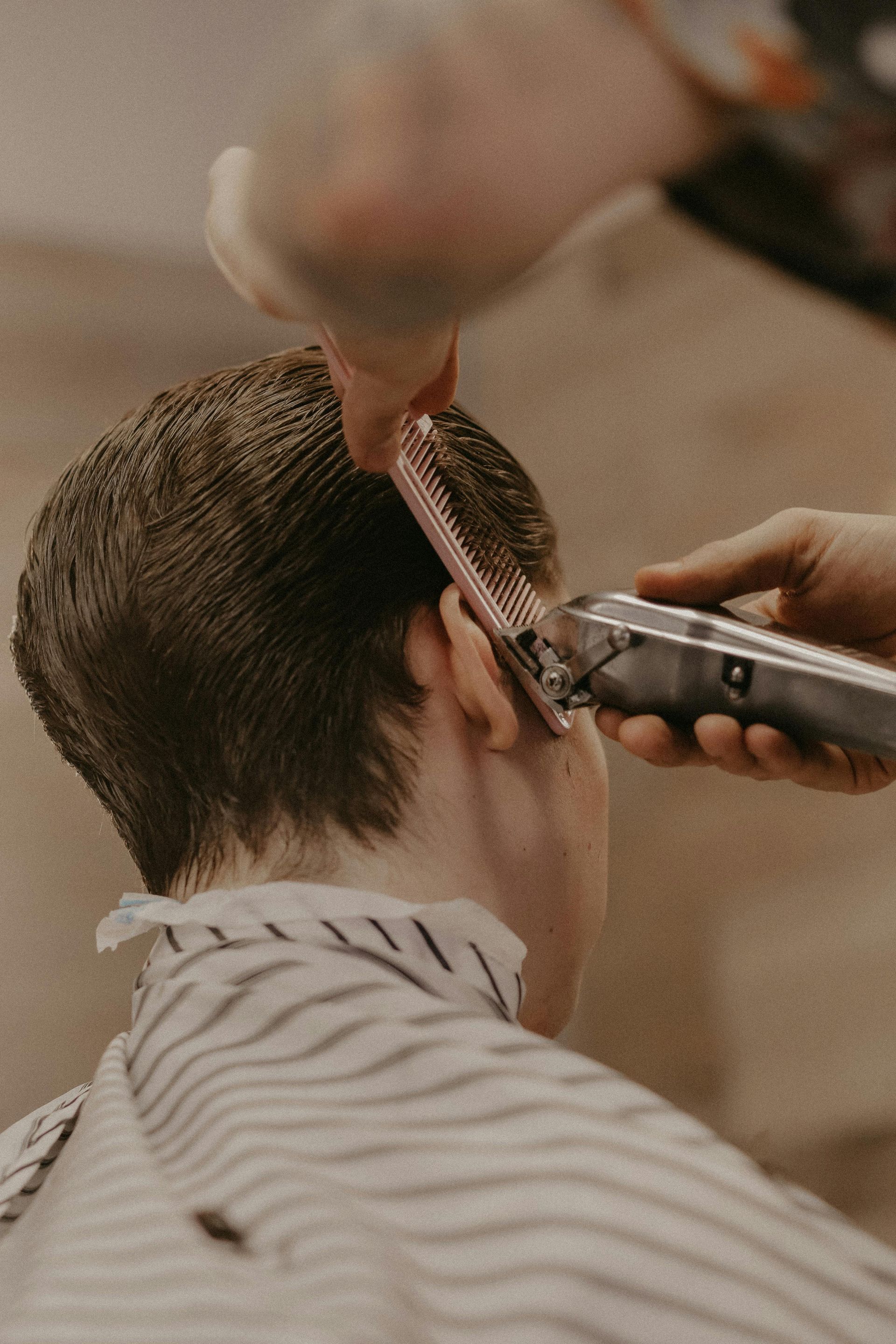 Un barbero utiliza una maquinilla y un peine para recortar el pelo alrededor de la oreja del cliente.