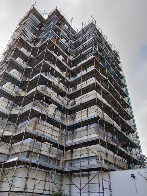 Grattacielo in costruzione con impalcature sullo sfondo di un cielo nuvoloso.