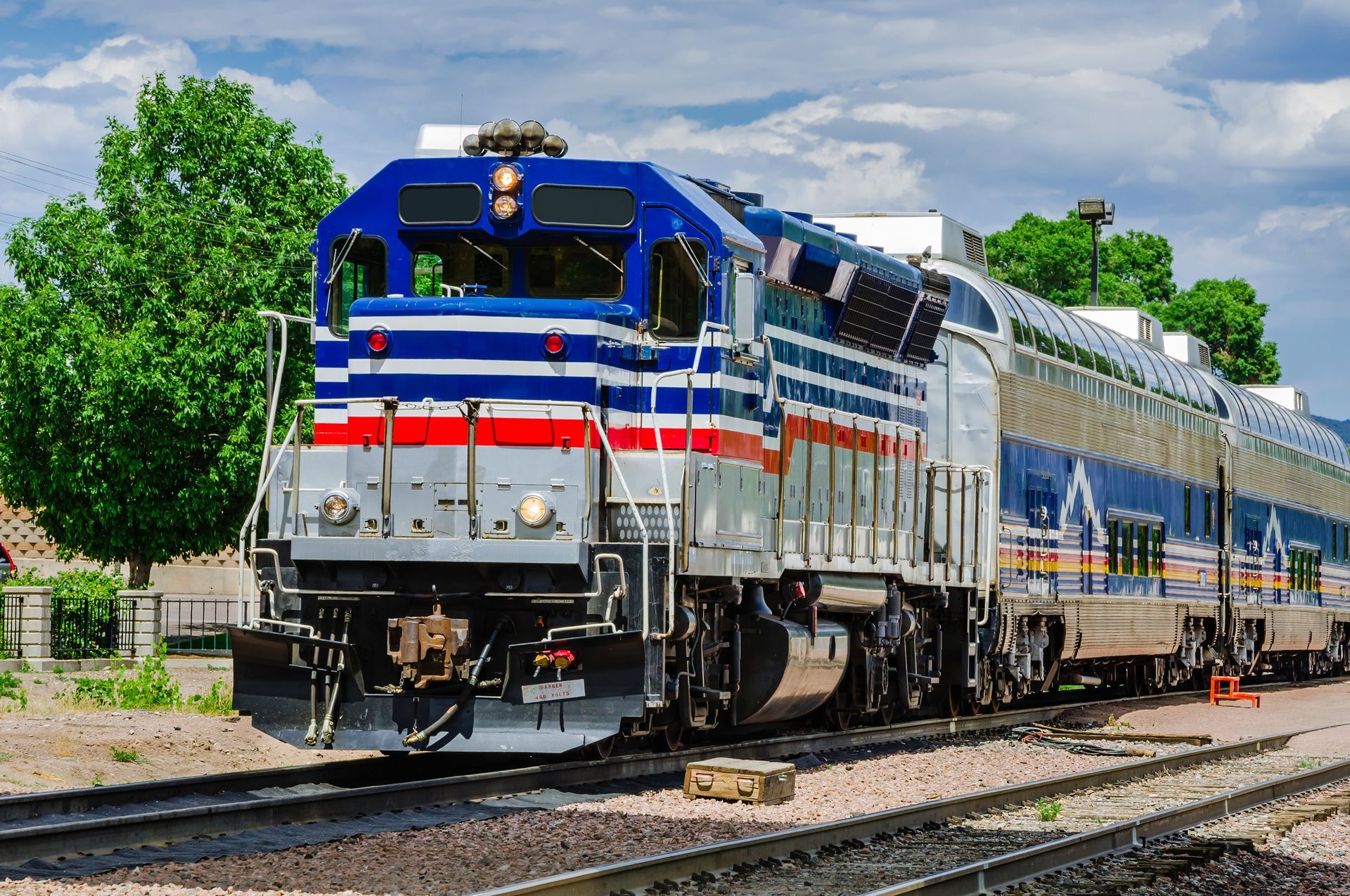 Blue, silver, and red passenger train on tracks, sunny day.