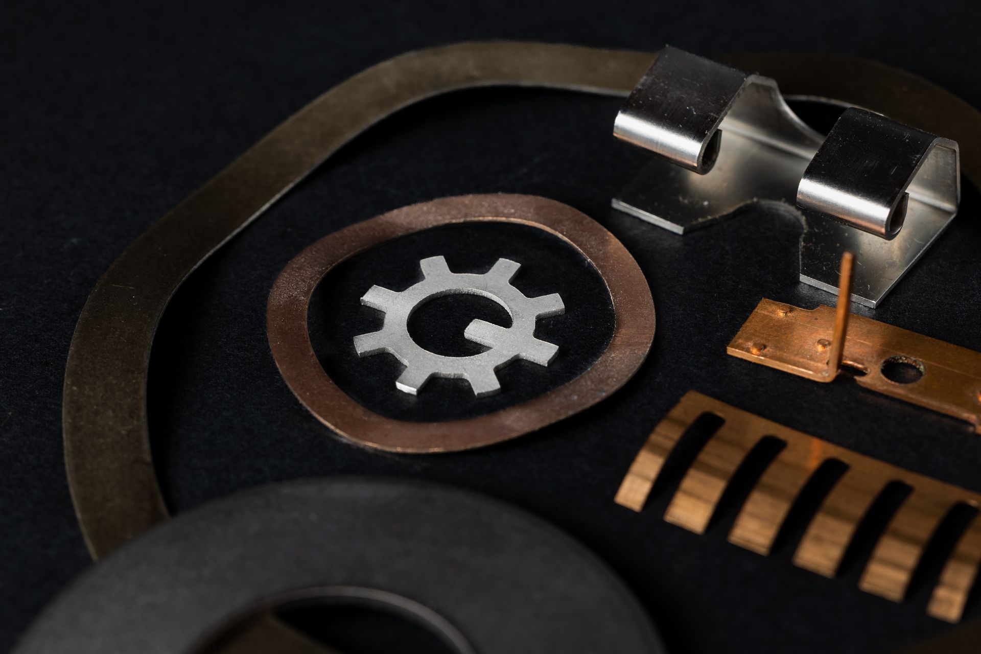 Close-up of various metal stamped parts, including washers, clips, and brackets, on a black background.