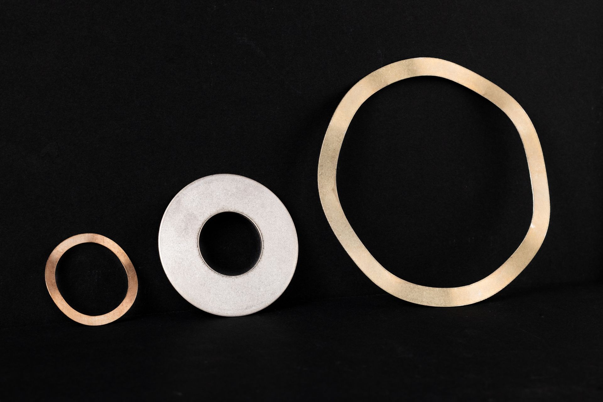 Three circular stamped metal discs of varying sizes on a black background.
