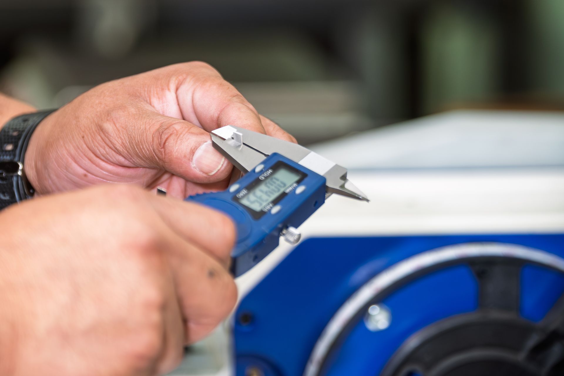 Person uses digital calipers to measure an object in a workshop, blue calipers.
