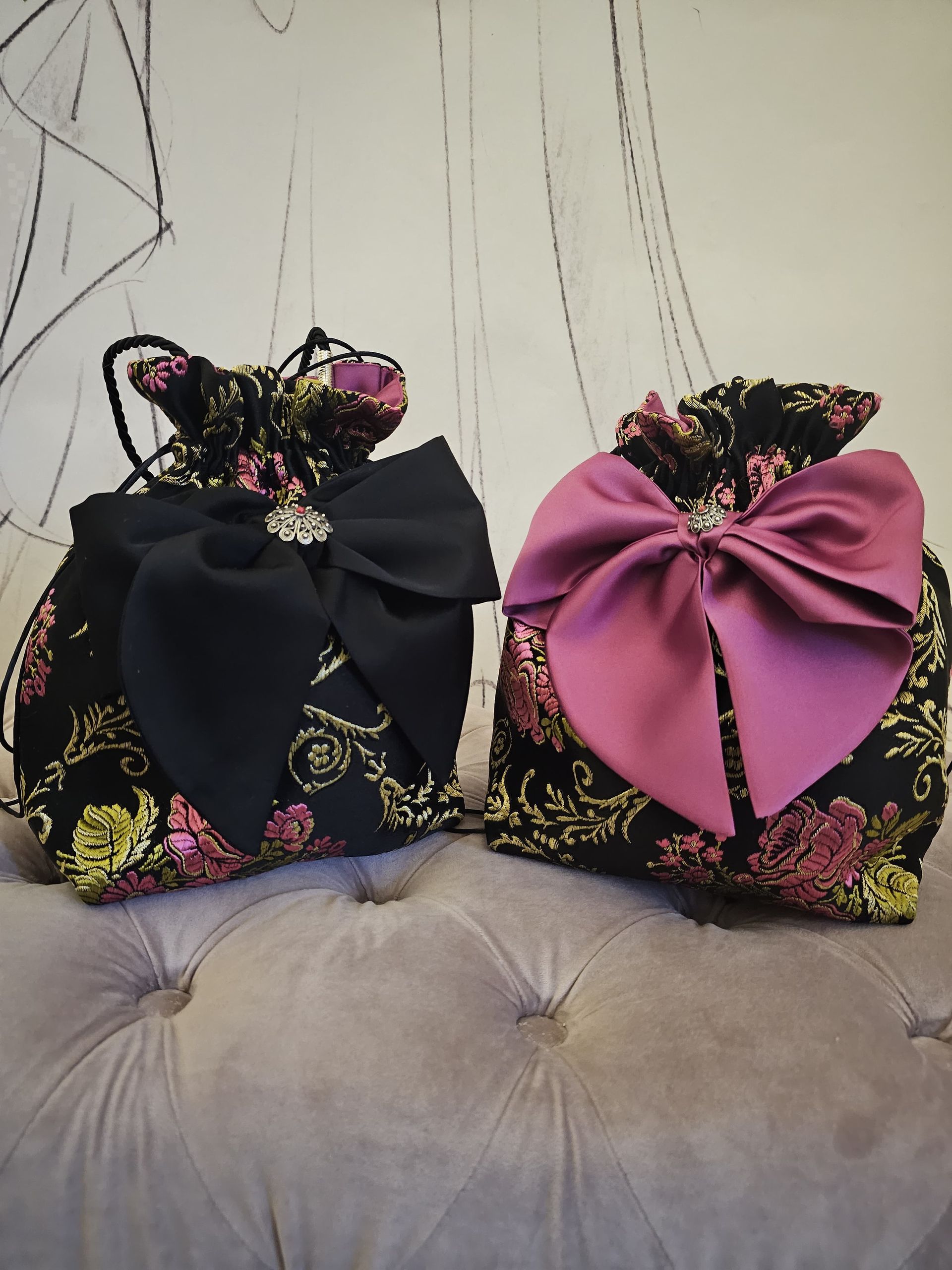 Una borsa nera con un fiocco rosa è seduta accanto a una borsa rosa
