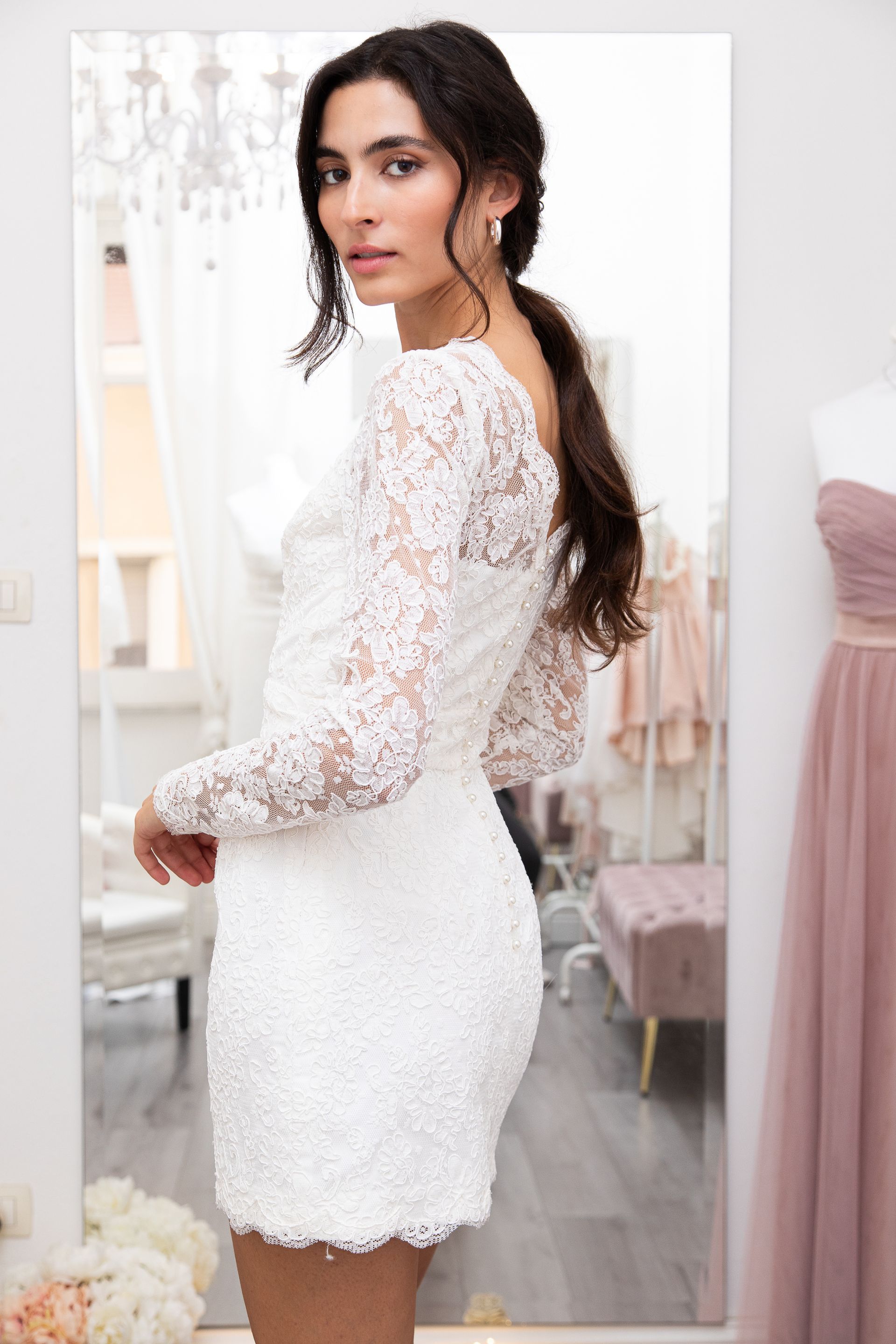 Una donna con un abito di pizzo bianco è in piedi davanti a uno specchio.