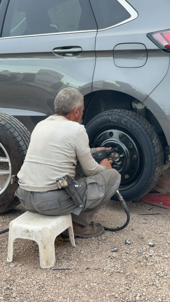 Man seated on a stool, using a tool to work on a car tire.