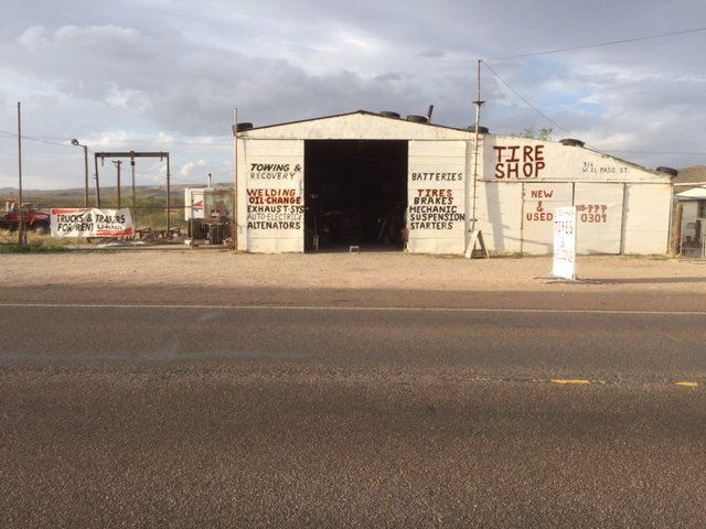 White tire shop building with open garage door and roadside sign, under cloudy sky.