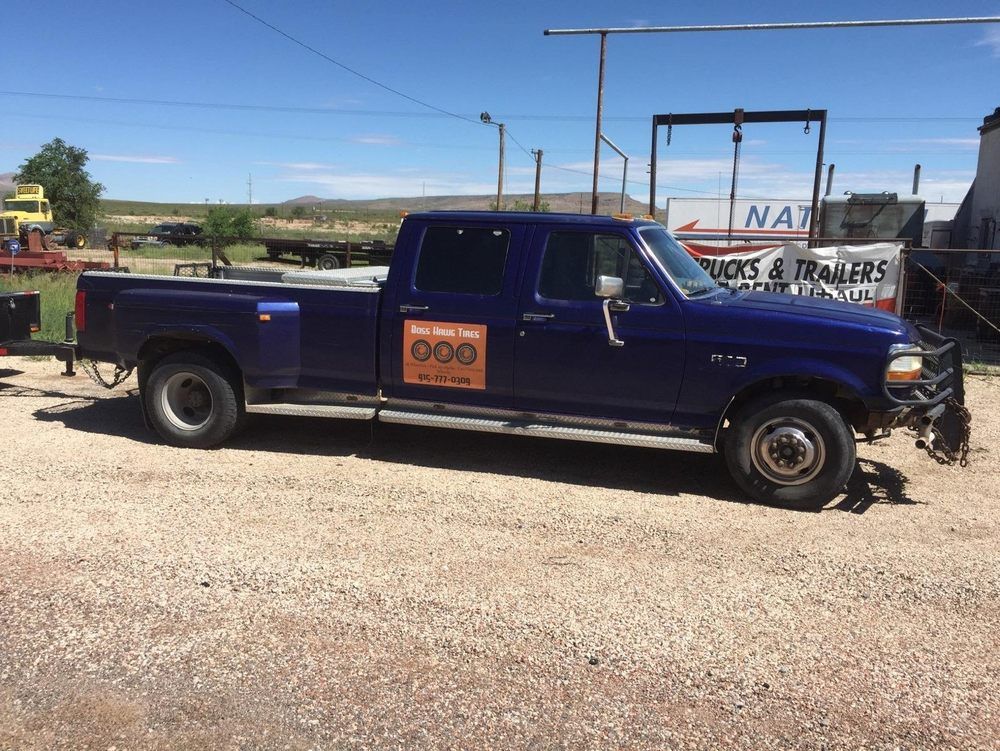 Blue Ford pickup truck with a large bed parked on gravel, near a sign for trucks and trailers.