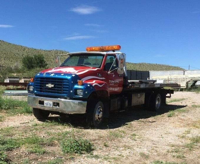 Tow truck with patriotic paint job, parked outdoors on a sunny day.