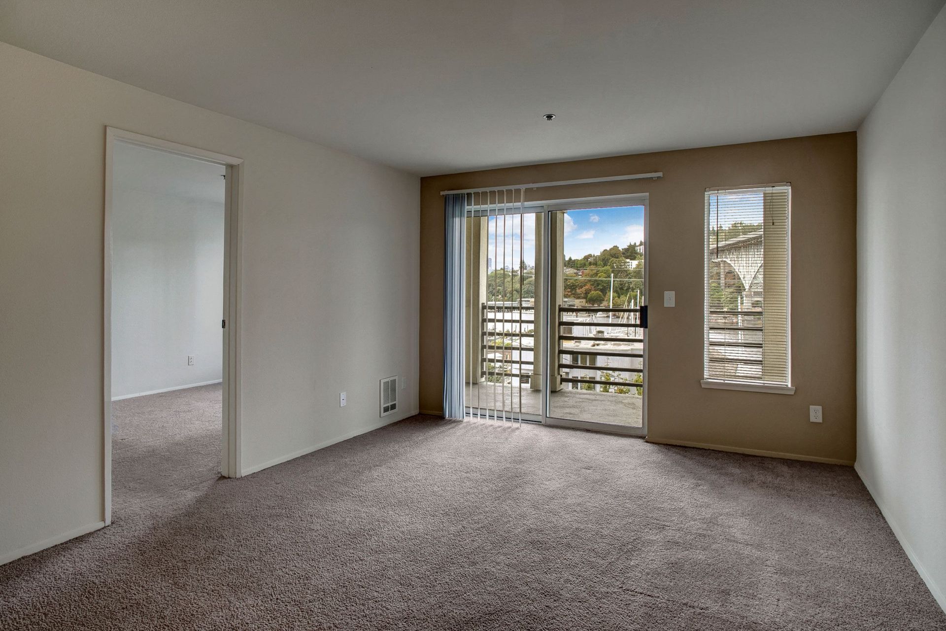 Empty room with carpet, a sliding glass door to a balcony, and a doorway to another room.