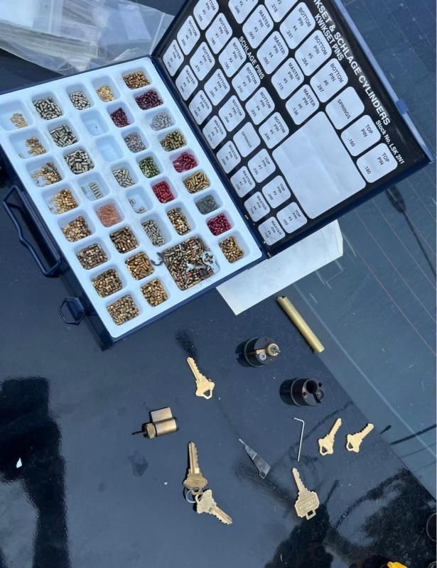 Open toolbox with small parts, keys, and black-and-gold hardware pieces on a floor.