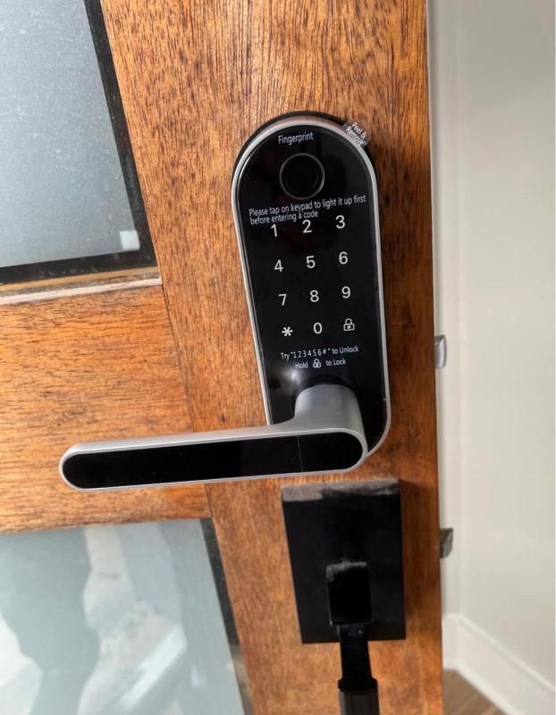 Black electronic keypad lock on a wooden door with a horizontal lever handle.