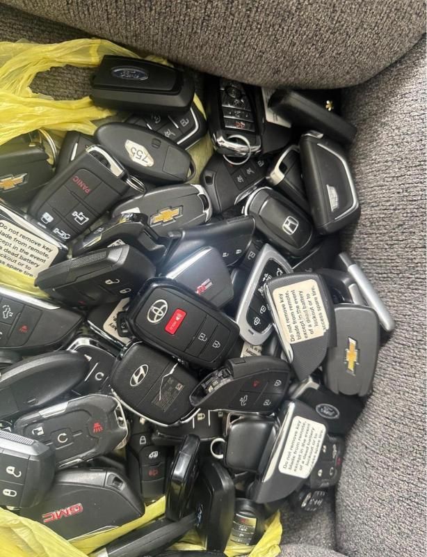 Pile of car key fobs in a gray fabric bin, mostly black with a few silver and red accents.