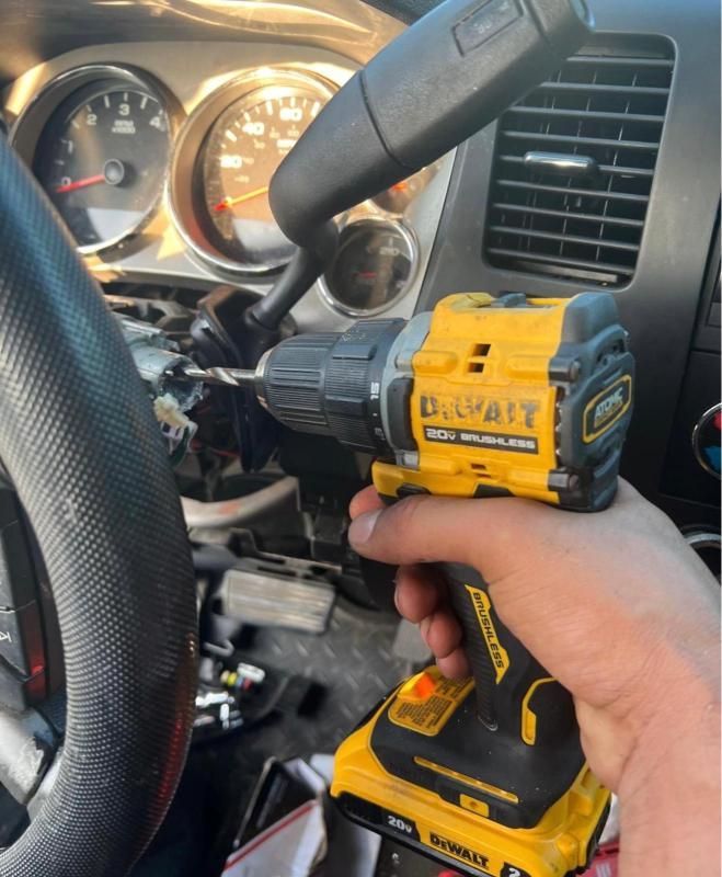 Hand holding a yellow DeWalt drill inside a car, aimed near the dashboard and steering wheel.