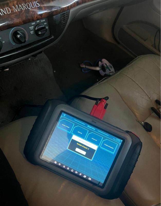 Tablet resting on a car seat, displaying a blue diagnostic-style screen with a red connector attached.