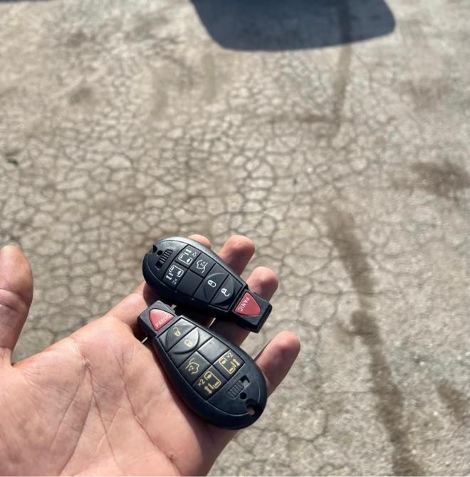 Two black car key fobs with red buttons resting in a person's open hand outdoors.