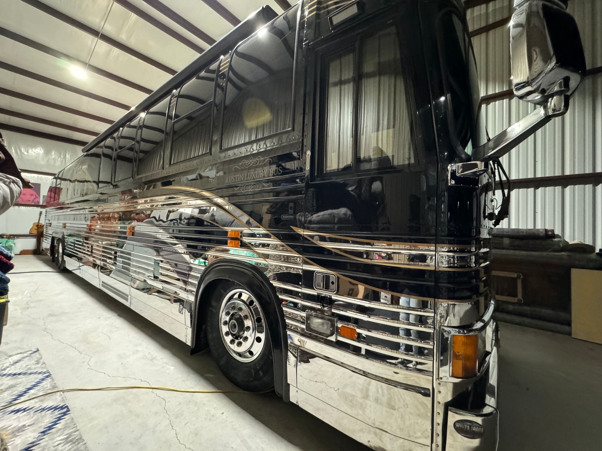 A large black and silver bus is parked in a garage.