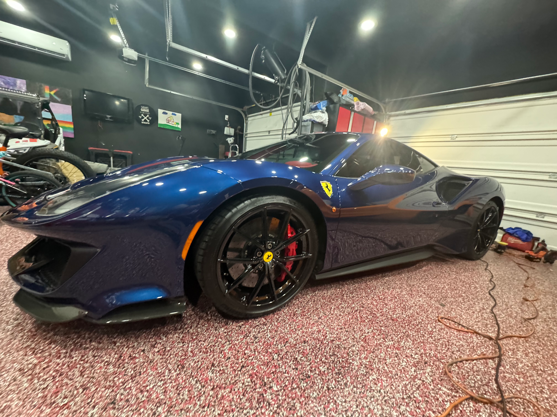 A blue ferrari 488 spider is parked in a garage.
