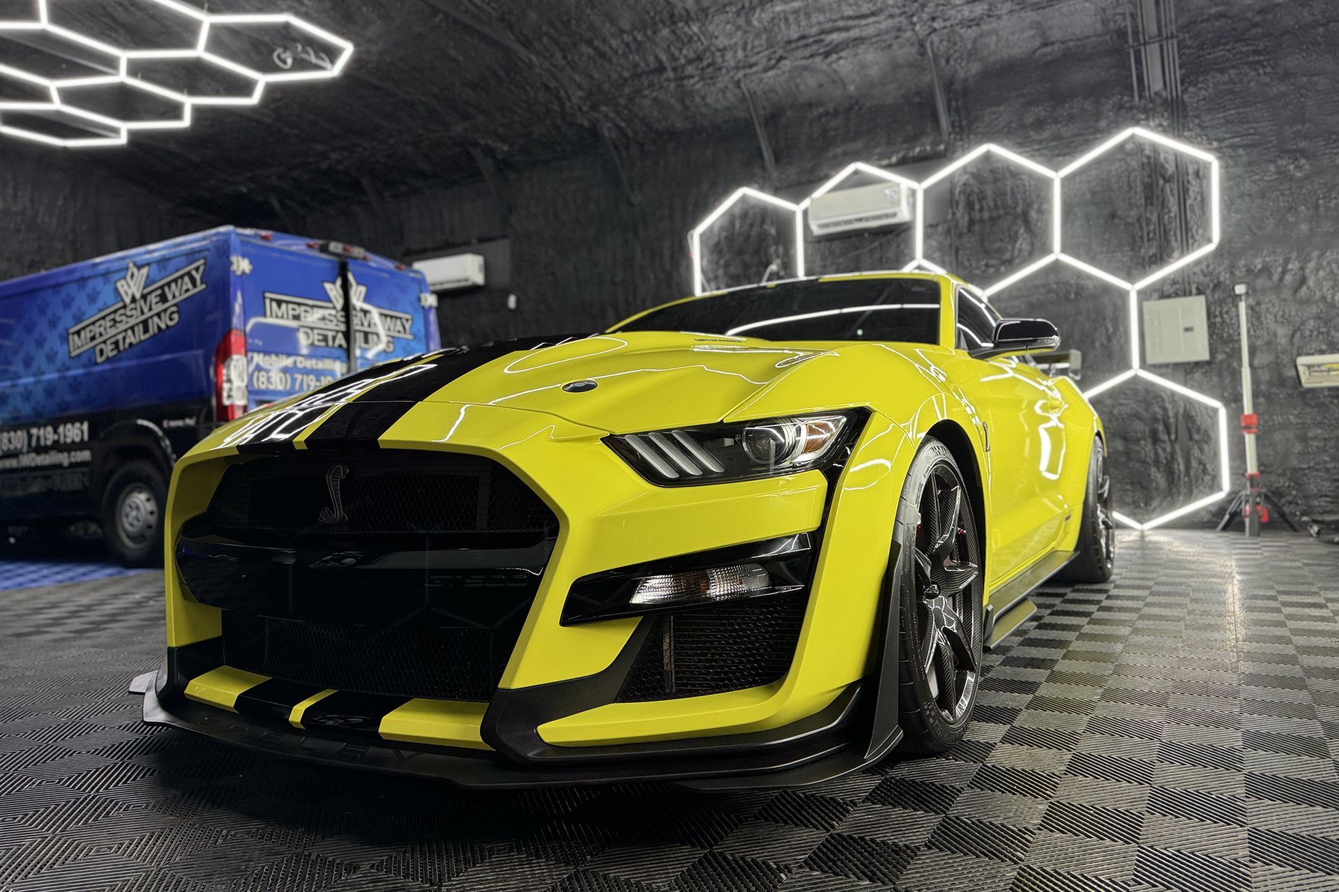 A yellow mustang is parked in a garage next to a blue van.