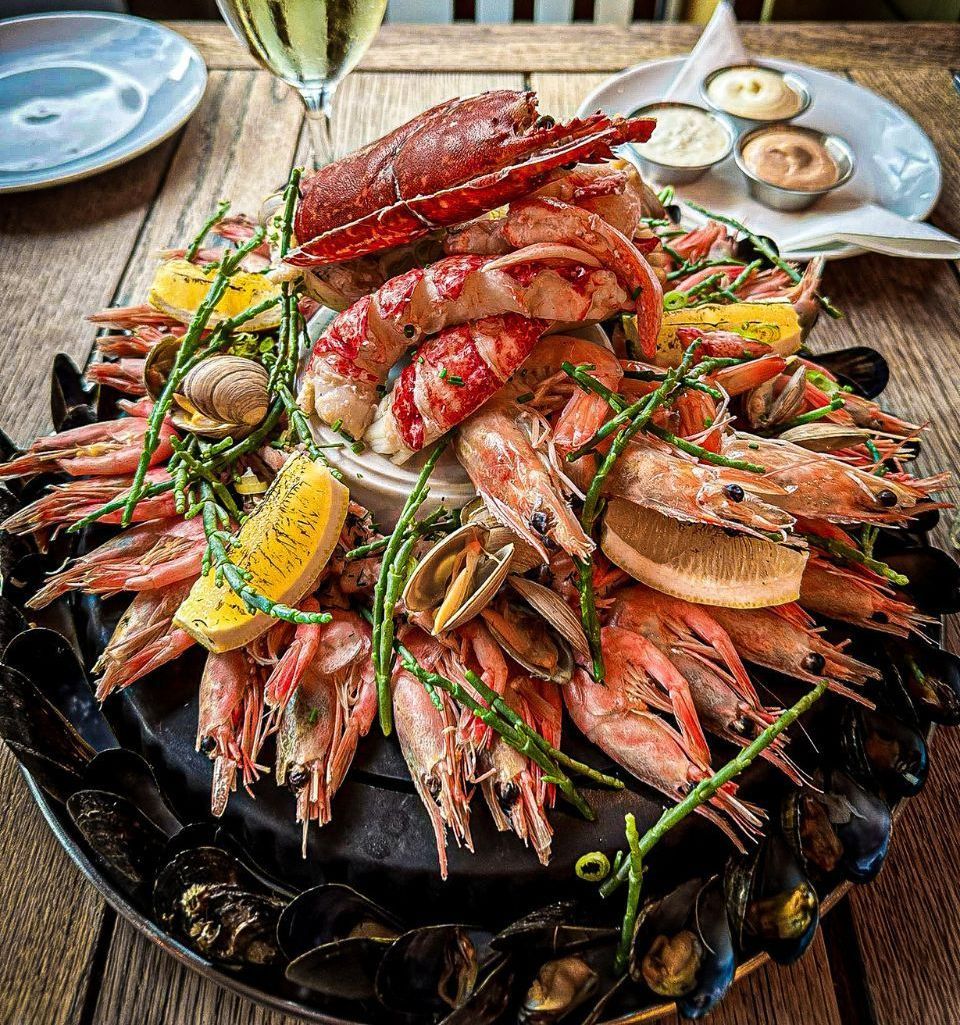 Seafood platter on a black plate, with a glass of white wine, and sauces on the side.