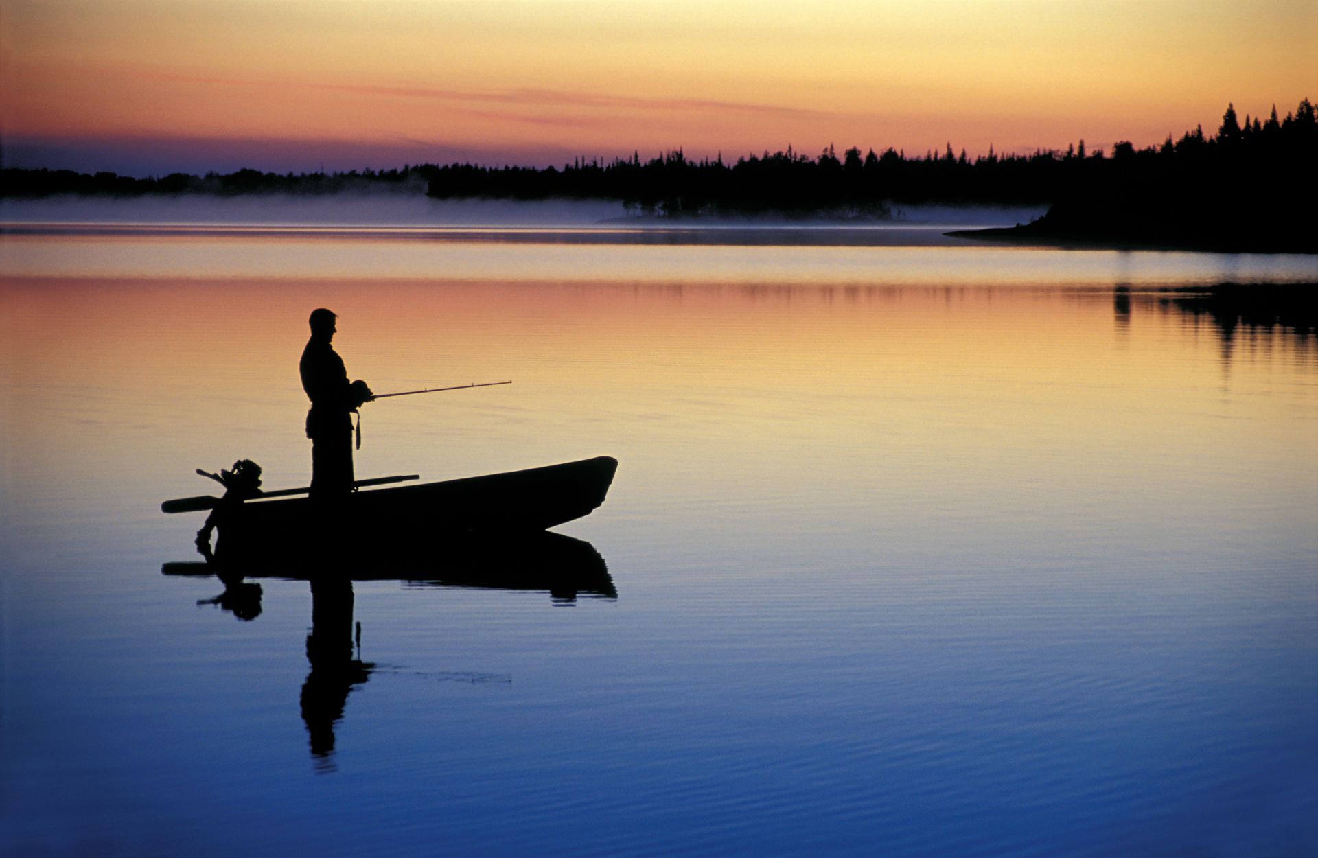 a man is fishing in a boat on a lake at sunset