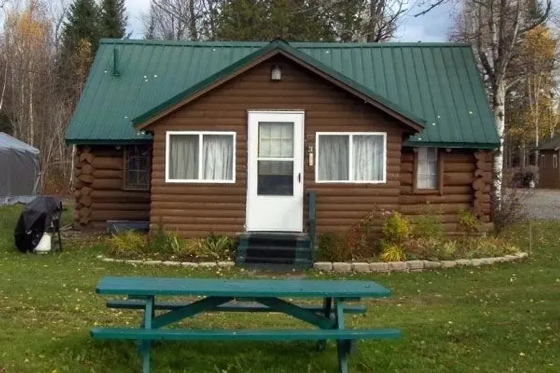 a small log cabin with a green roof and a picnic table in front of it .