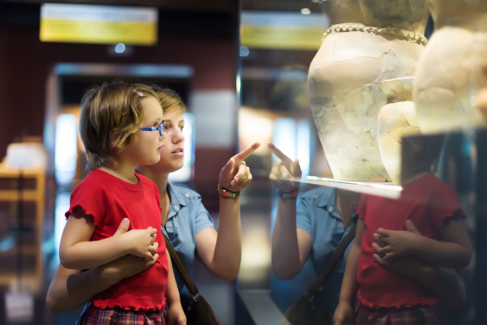 a woman and a little girl are looking at a vase in a museum .
