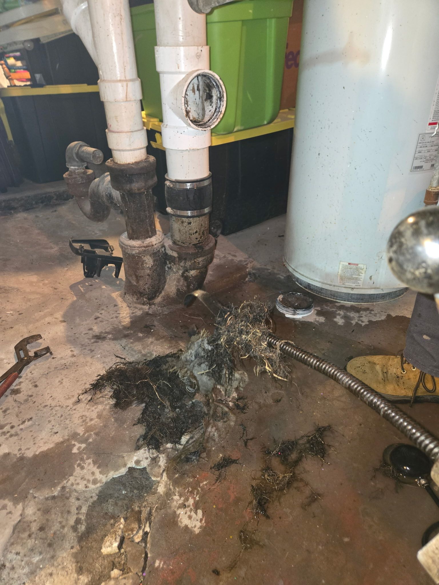 A water heater is sitting on the floor next to a pipe.