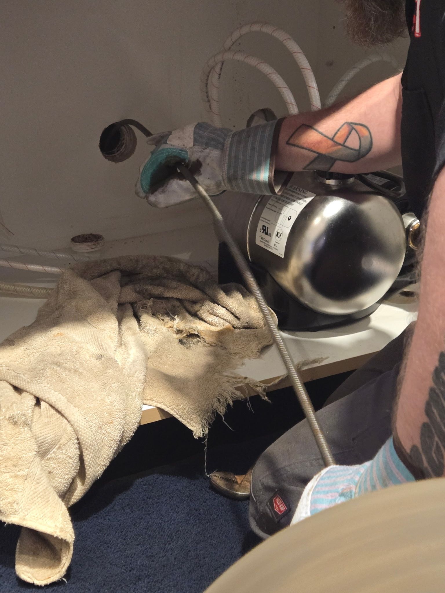 A man with a tattoo on his arm is using a vacuum cleaner to clean a toilet.