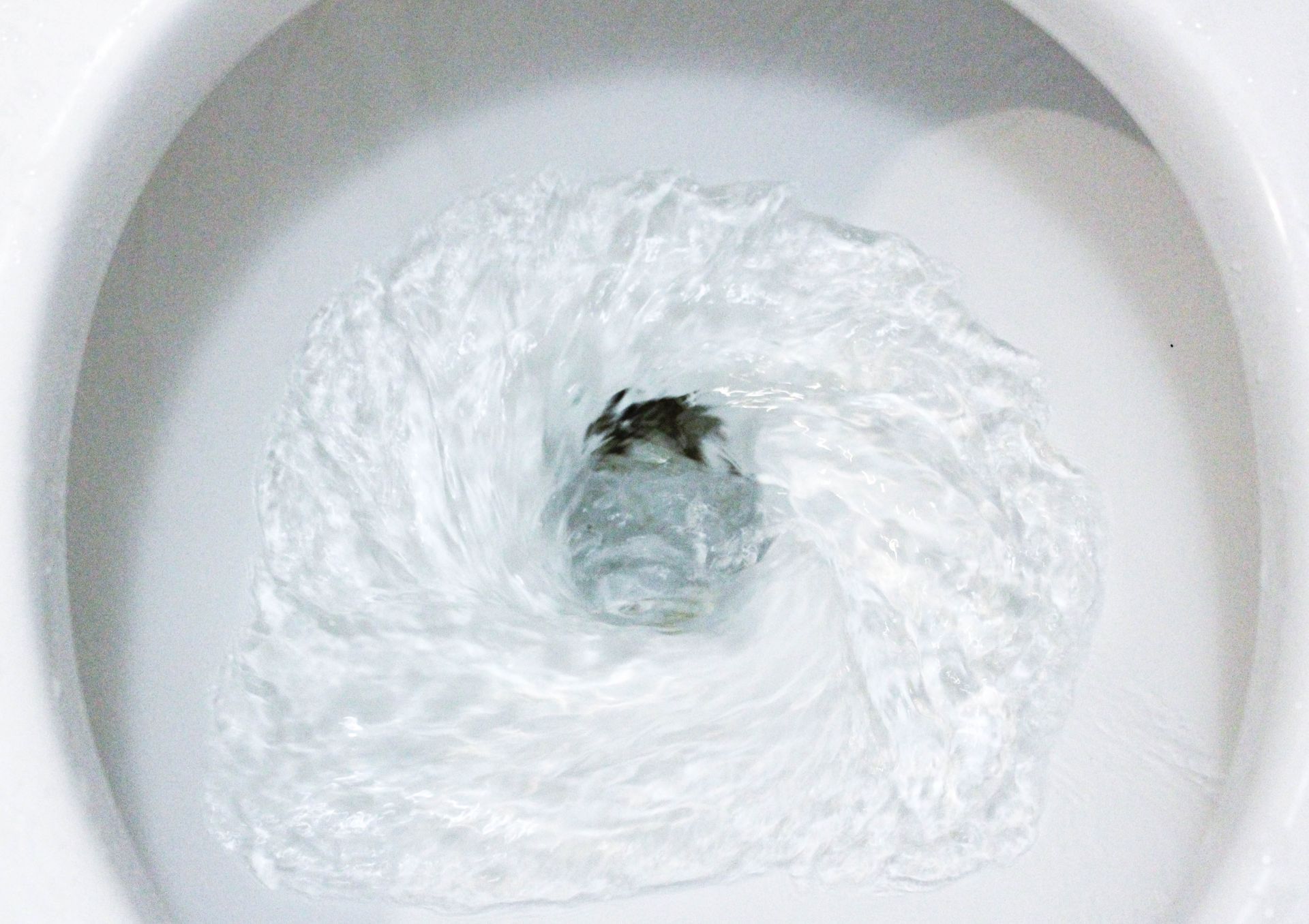 Top-down view of swirling water draining into a white sink or toilet bowl.