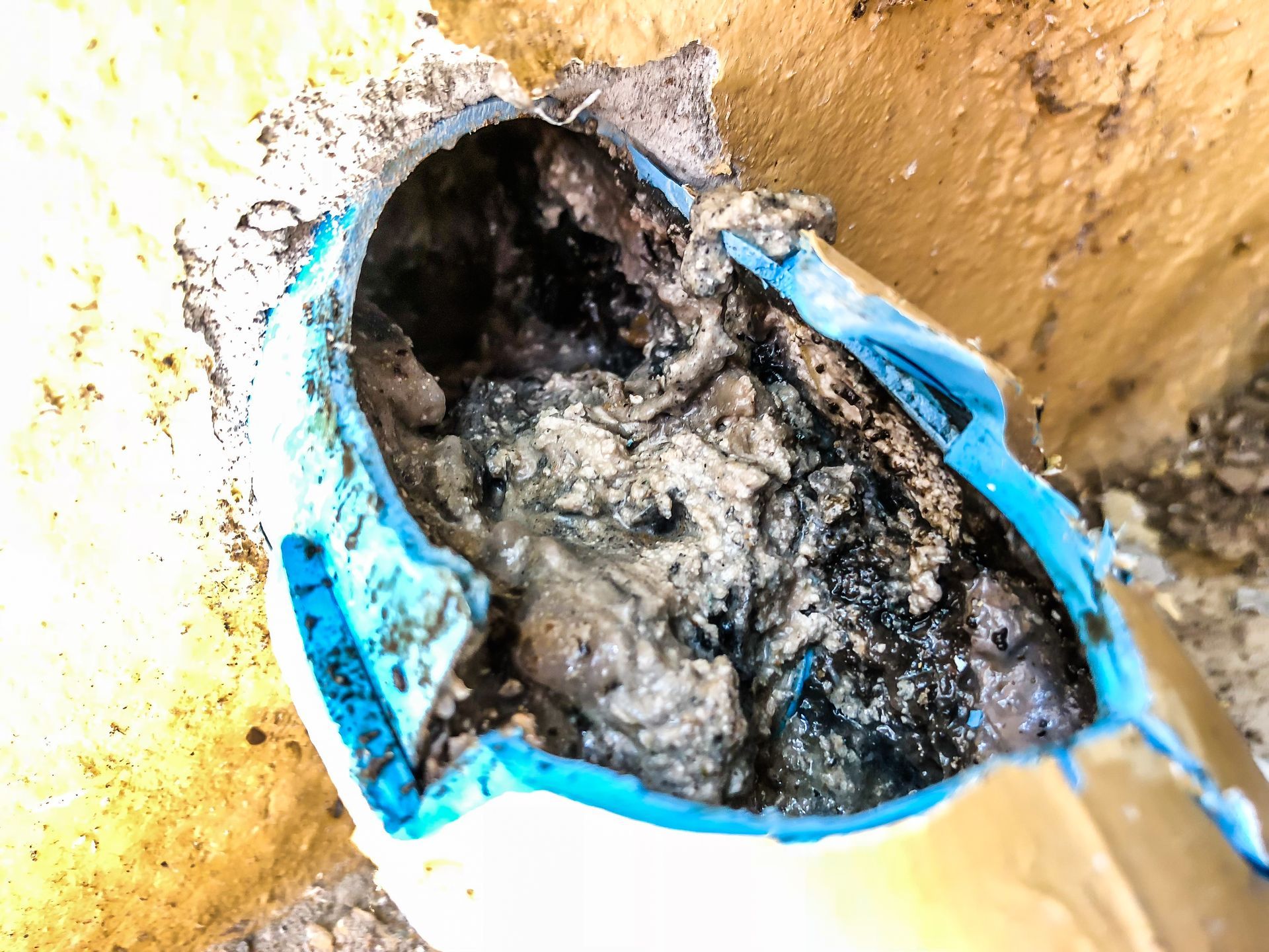 Broken blue pipe with heavy black mold or sludge against a stained yellow wall