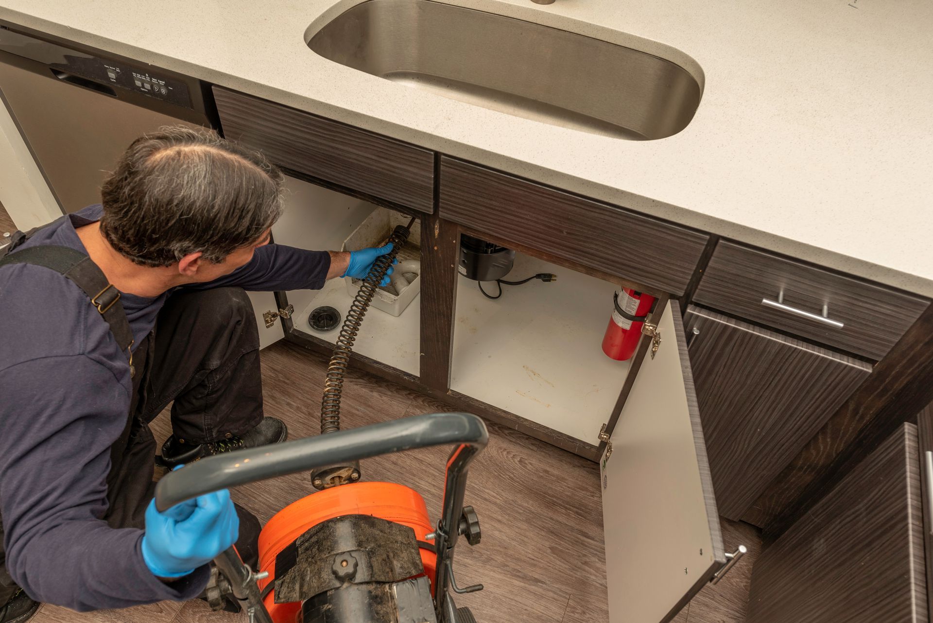 Technician working under a sink cabinet, using tools to repair plumbing.