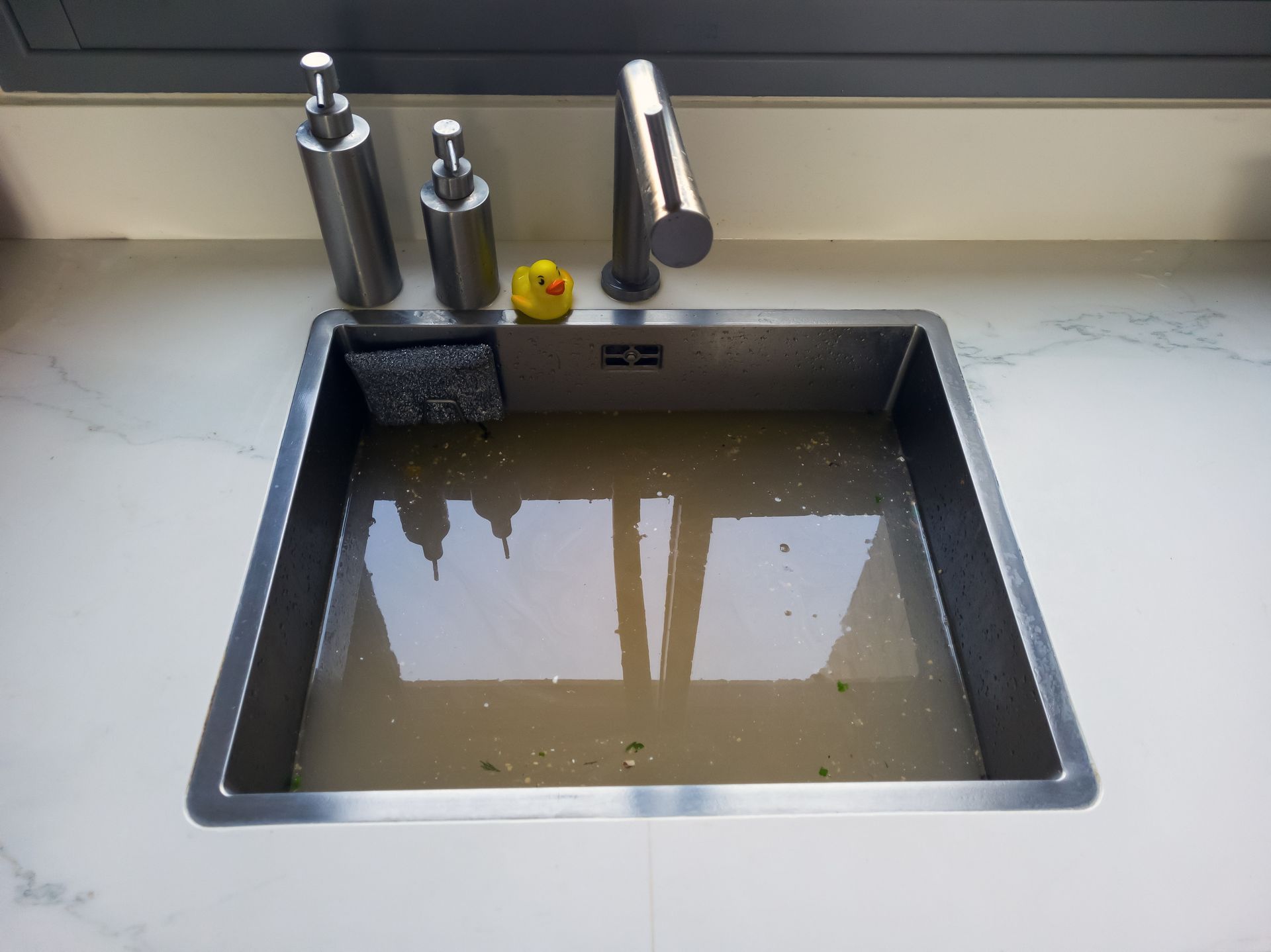 Modern kitchen sink with stainless faucet and soap dispenser, reflecting a bright window.