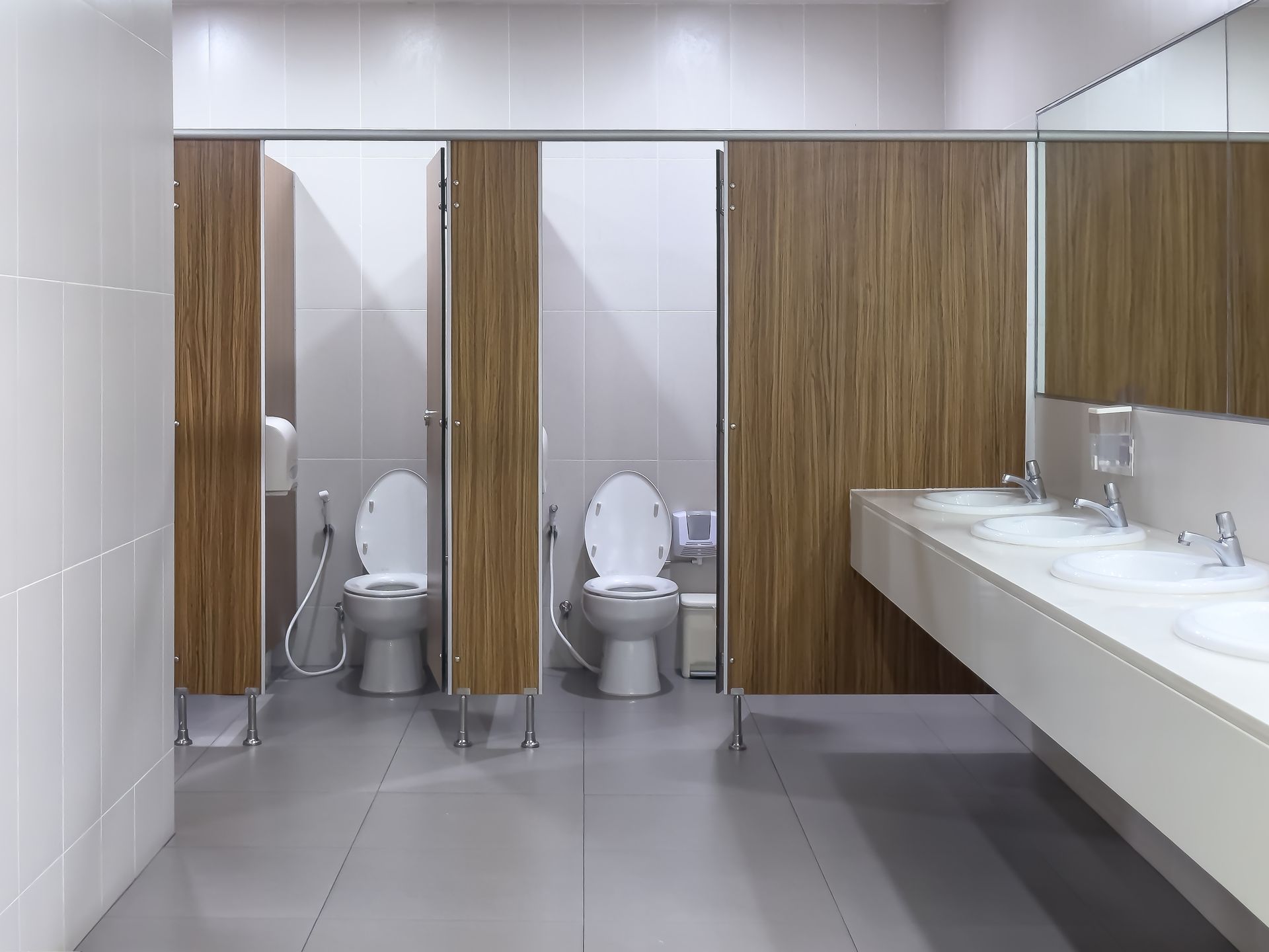 Public restroom with two toilet stalls and a row of sinks along a white counter.