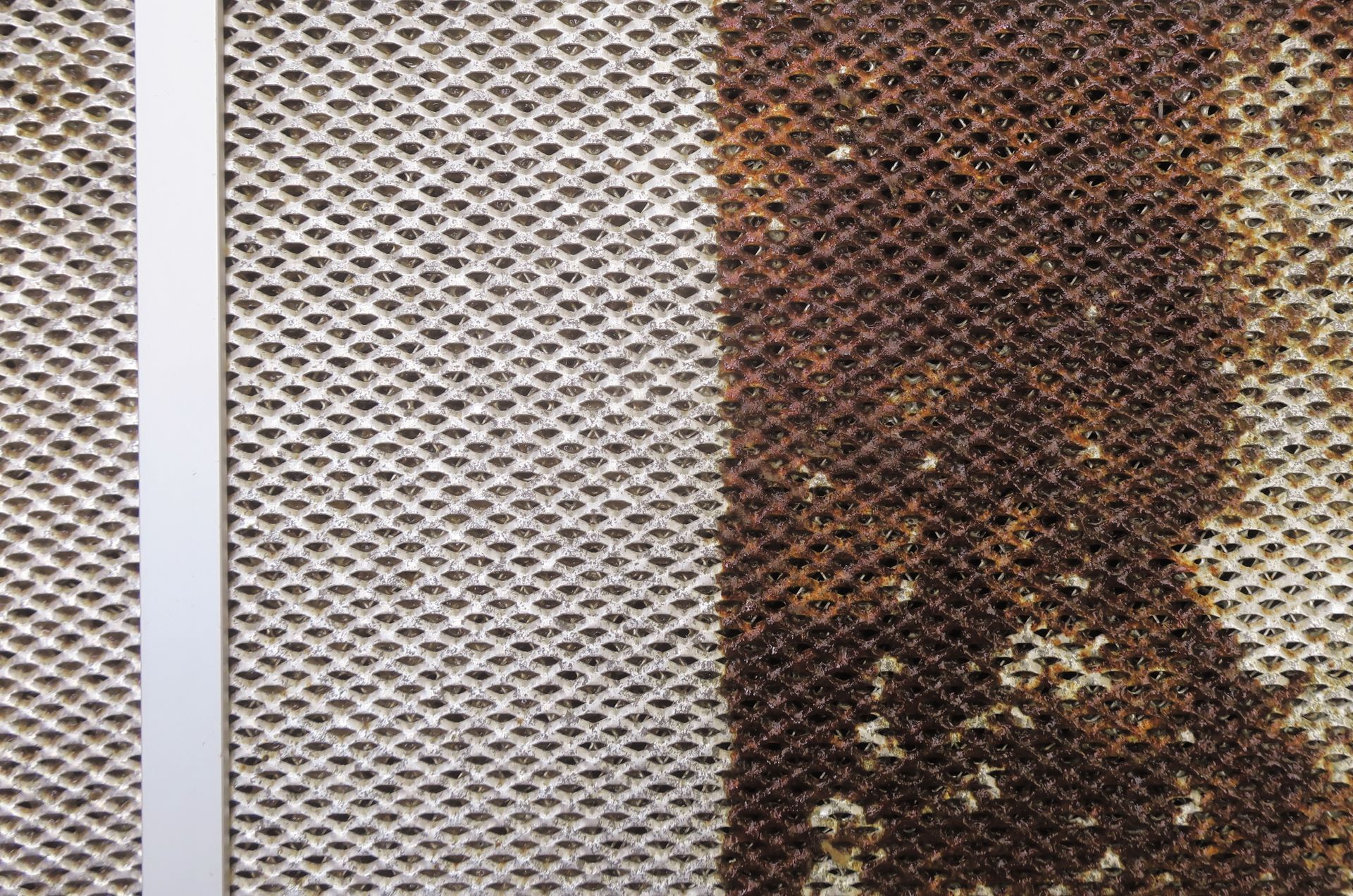 Close-up of a metal mesh screen with white and rusted brown sections.