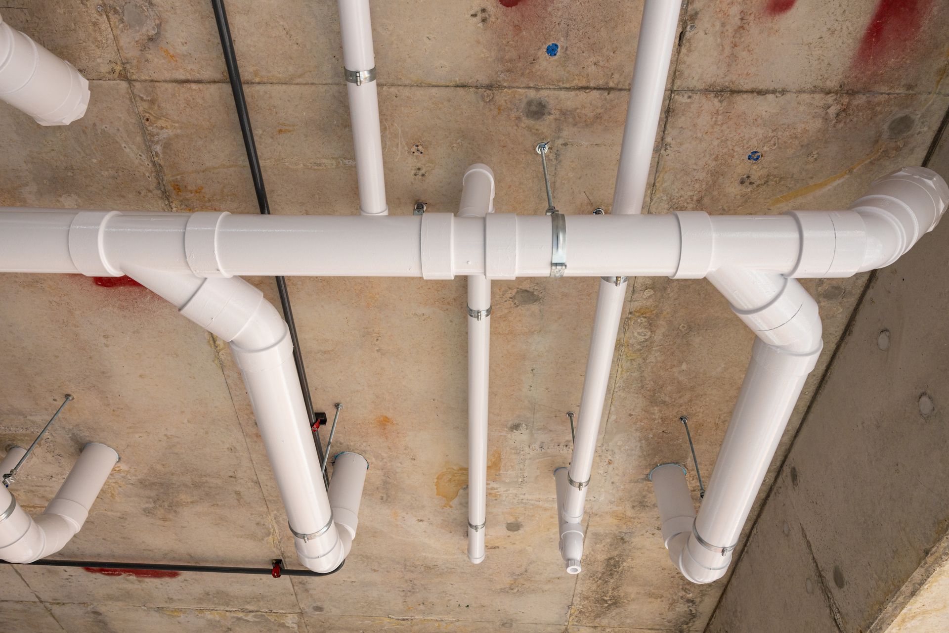 White PVC pipes and valves running across an unfinished ceiling with exposed concrete and utility lines.