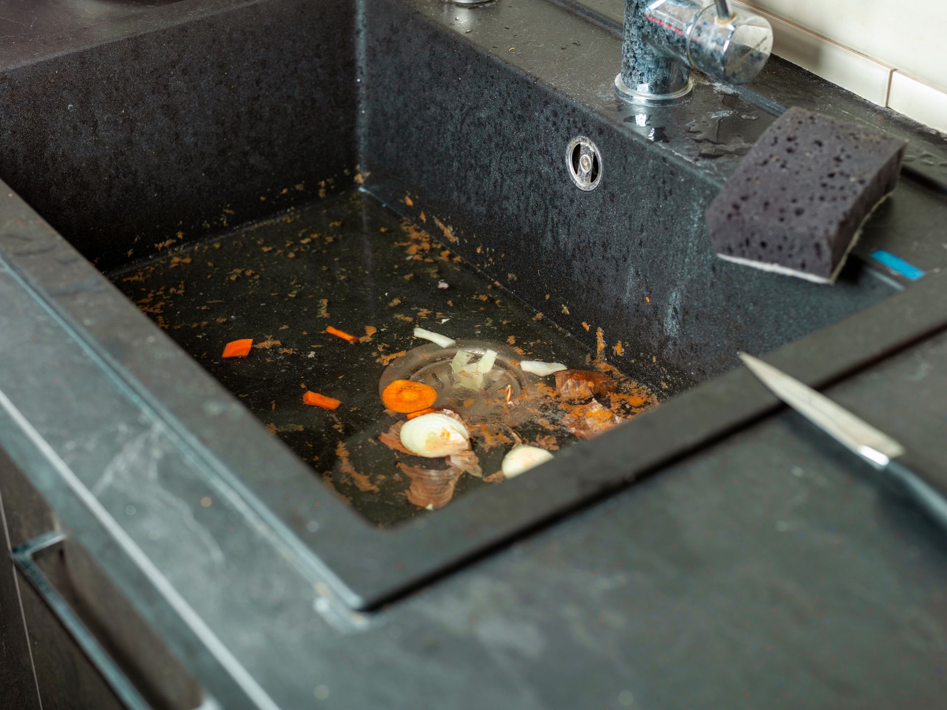 Dirty kitchen sink with leftover food scraps and a sponge under the faucet