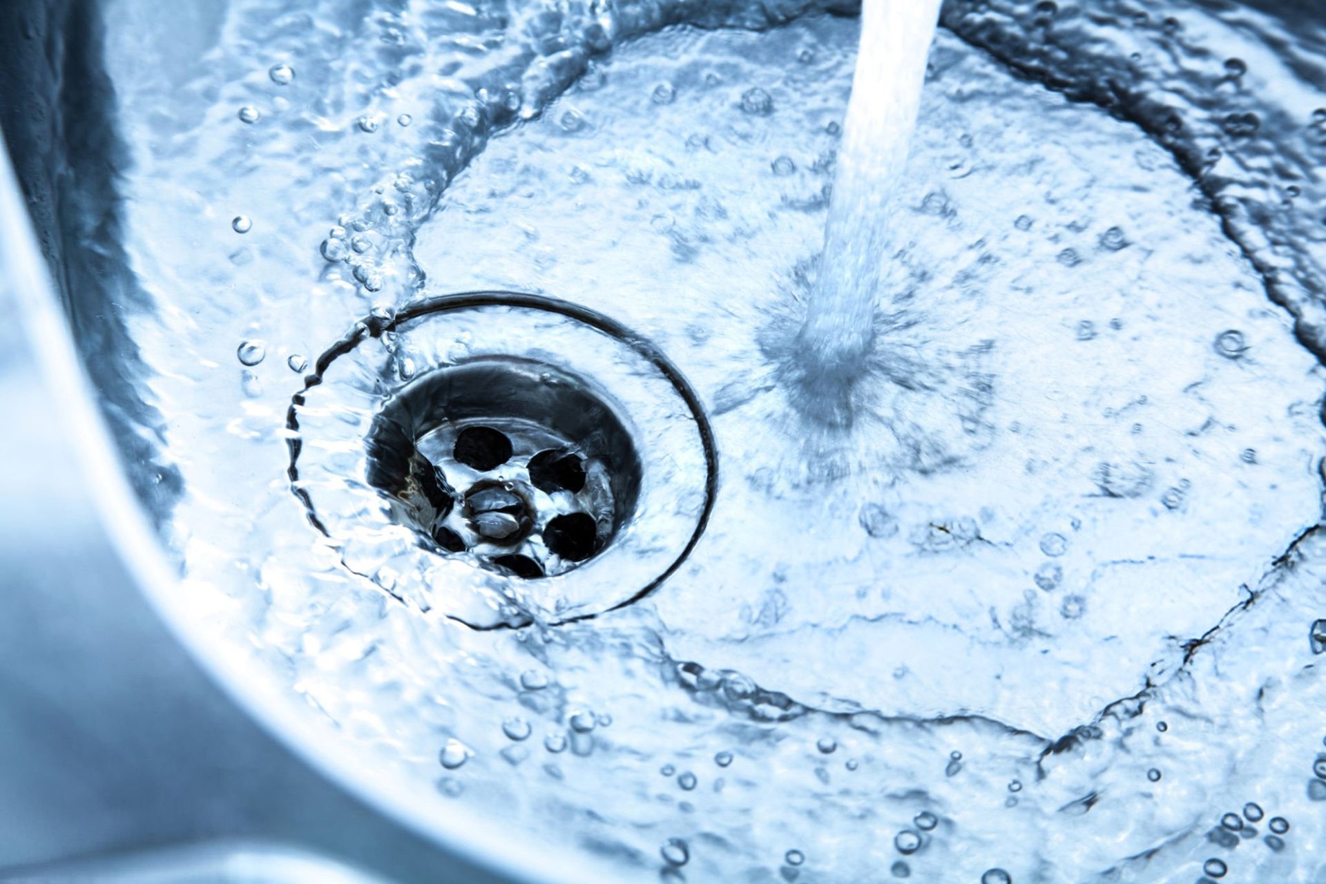 Close-up of water draining from a stainless steel sink, with swirling bubbles and a wet basin