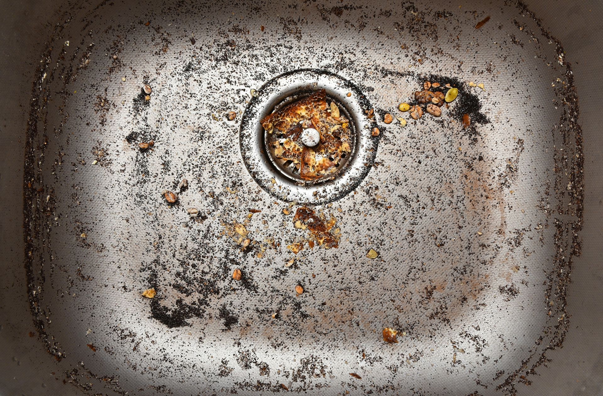 Rusty, dirty sink basin with a drain and scattered debris