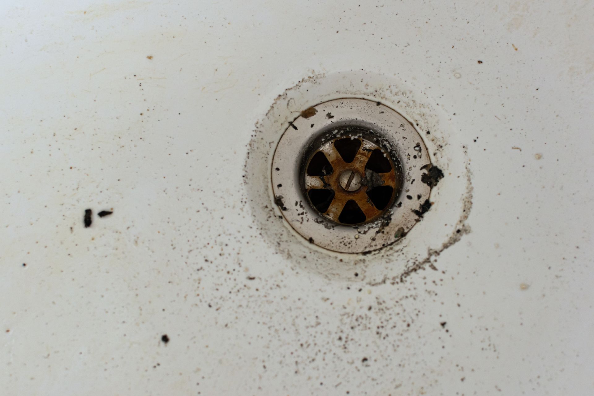Close-up of a dirty sink drain with rust stains and a black drain cover
