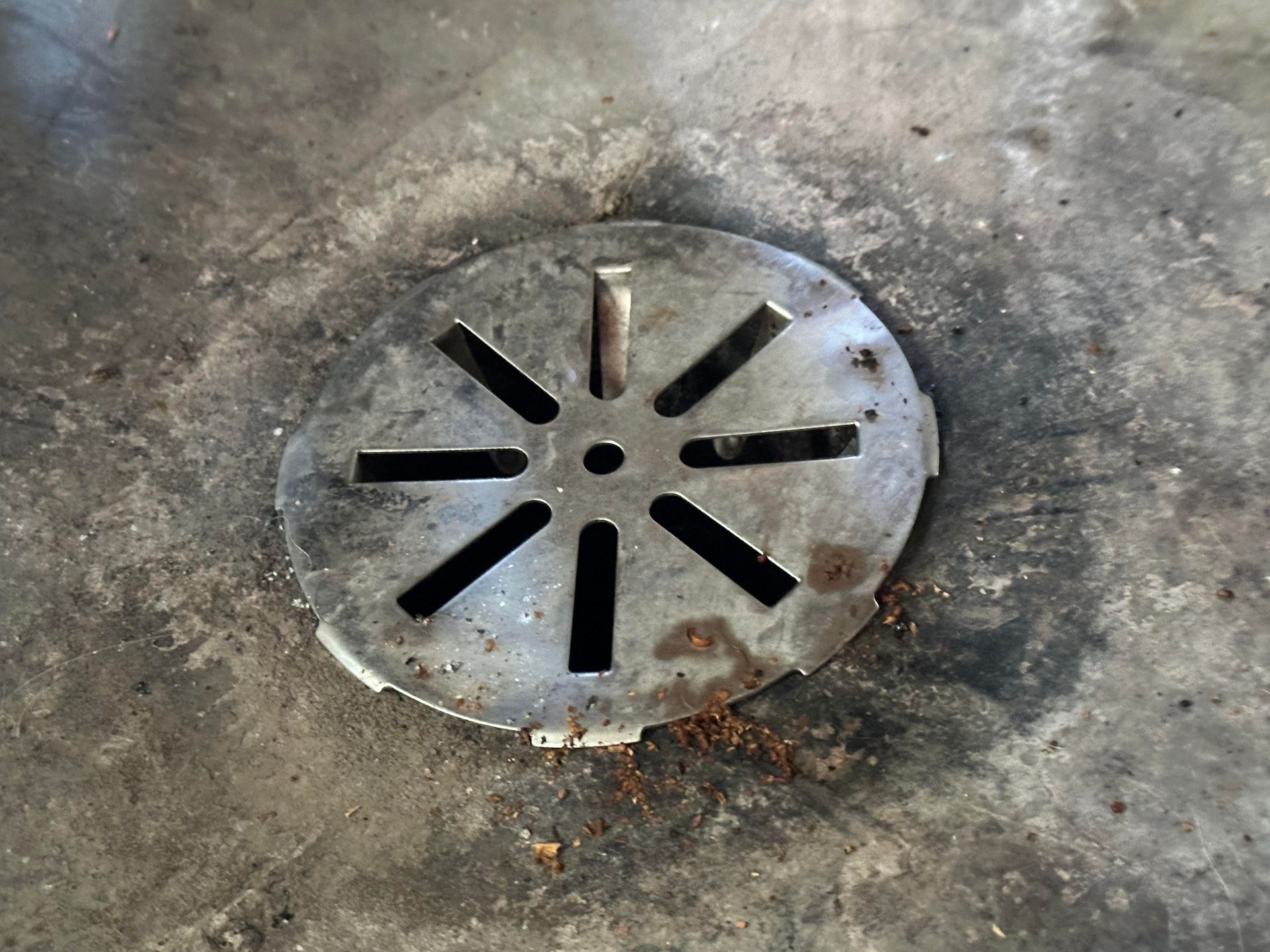 Round metal floor drain grate with black slots on a concrete surface