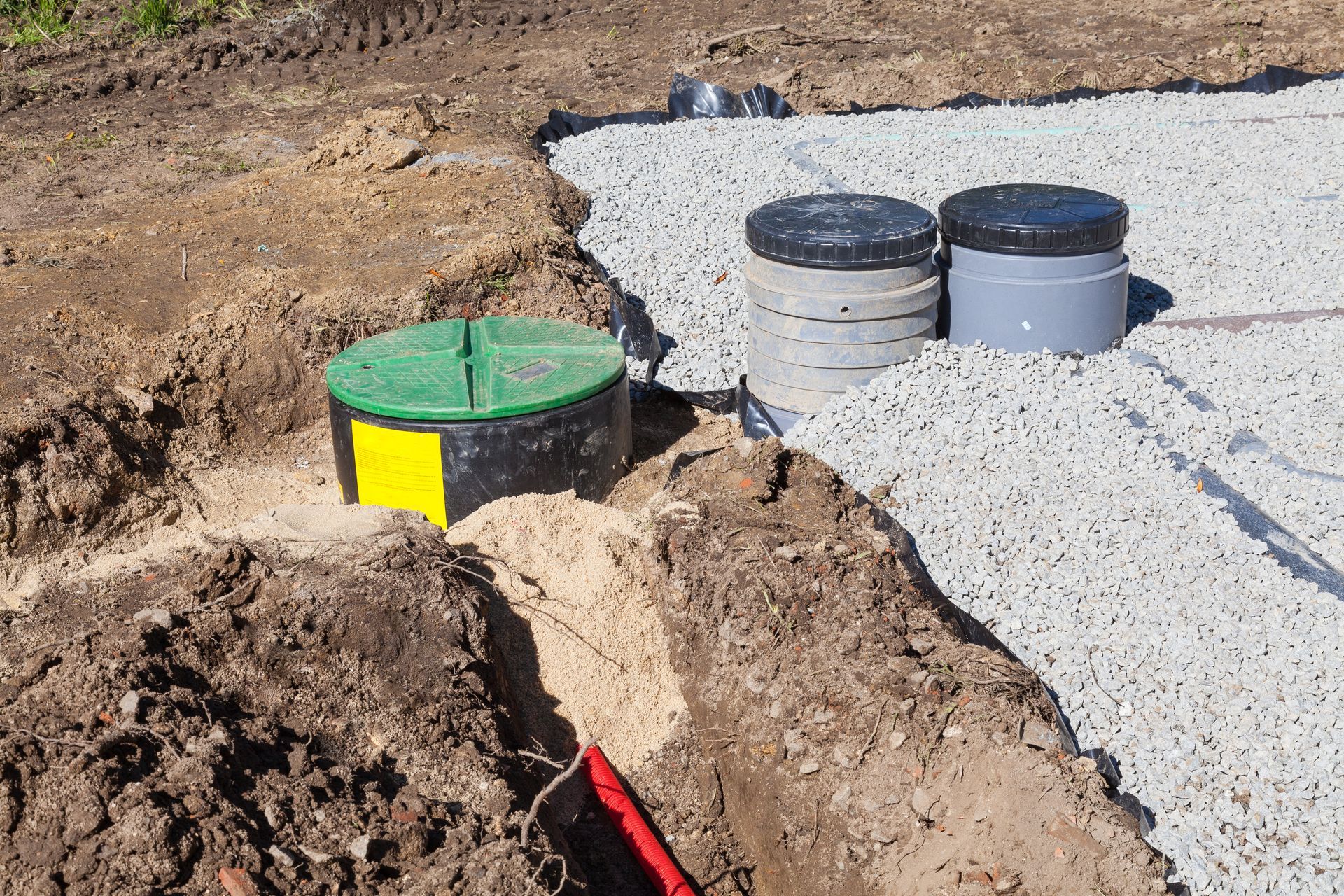 Construction site with underground utility tanks and exposed dirt trenches beside a gravel area