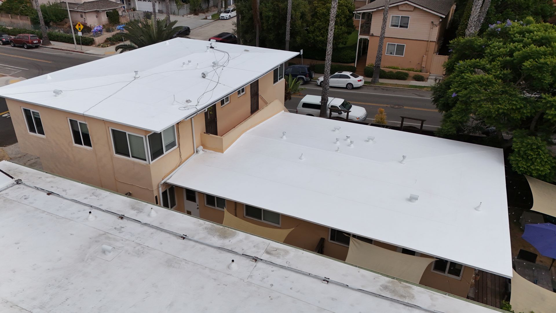 An aerial view of a two-story apartment building with a brown roof and green exterior, surrounded by trees and parked cars.
