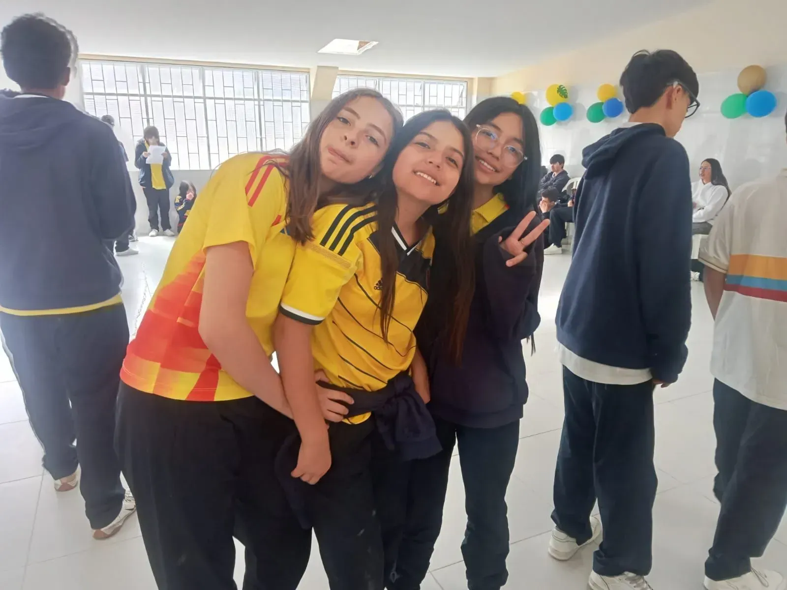 Tres personas sonriendo y posando juntas en una habitación interior decorada con globos.