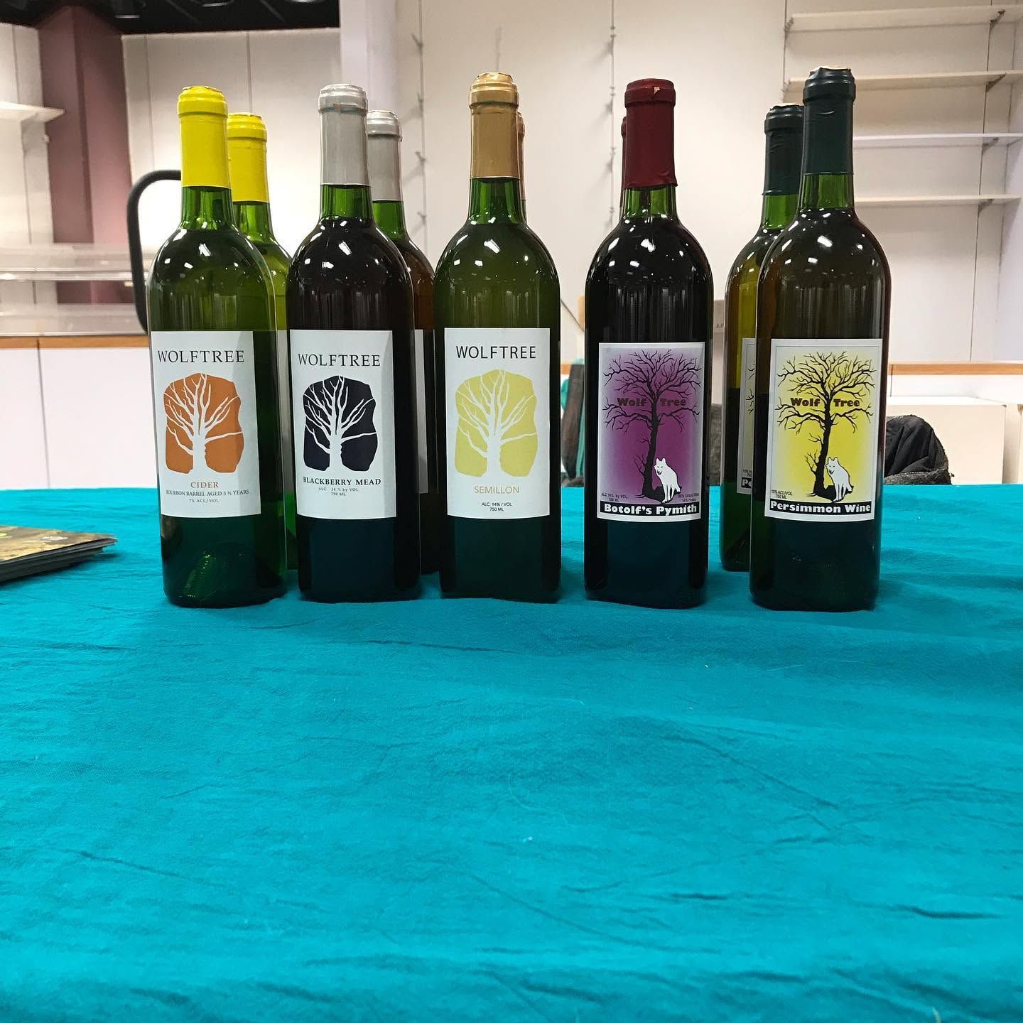 Five assorted bottles of olive oil with colored labels on a turquoise table indoors