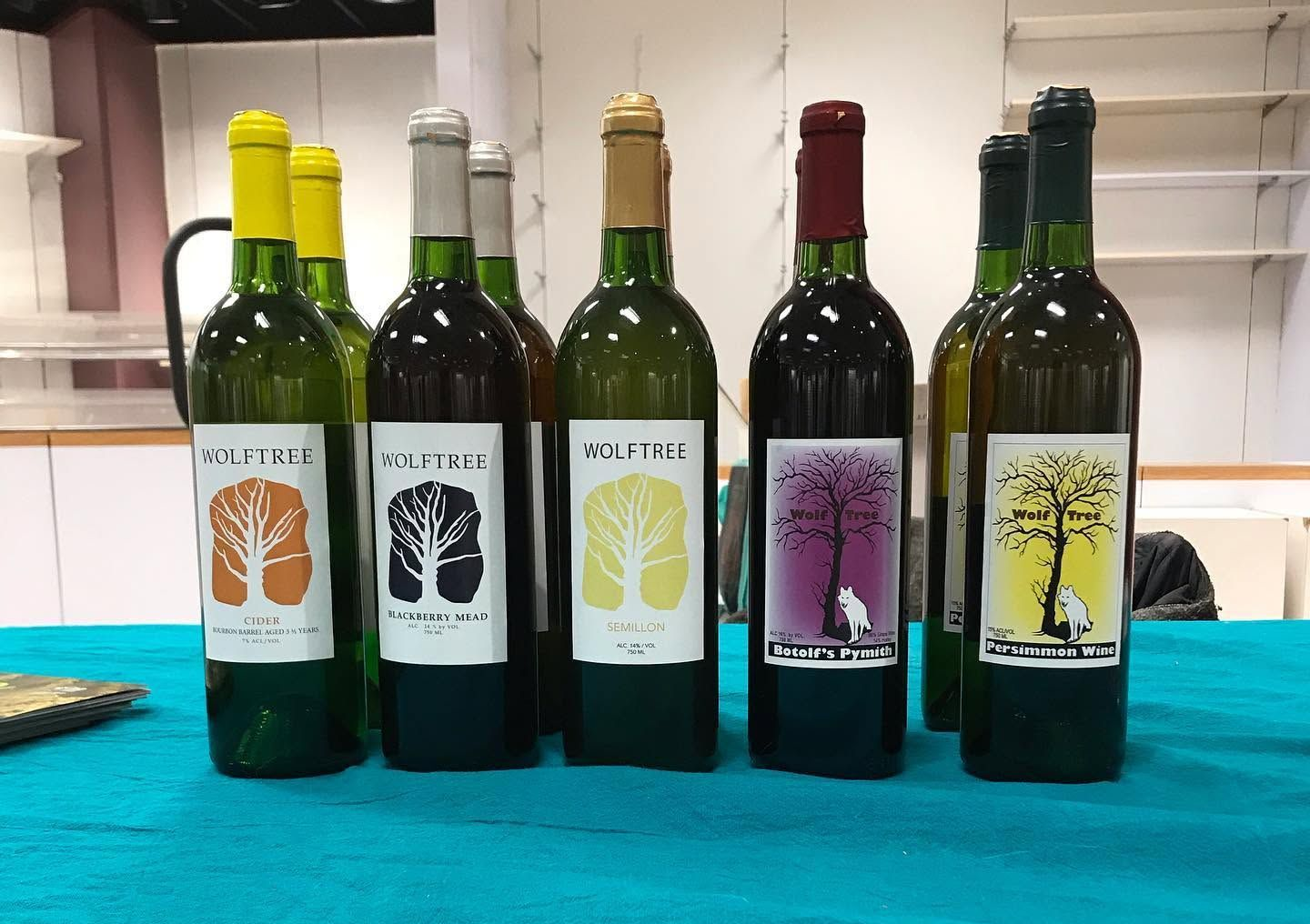 Five wine bottles on a turquoise table, each with colorful tree labels.