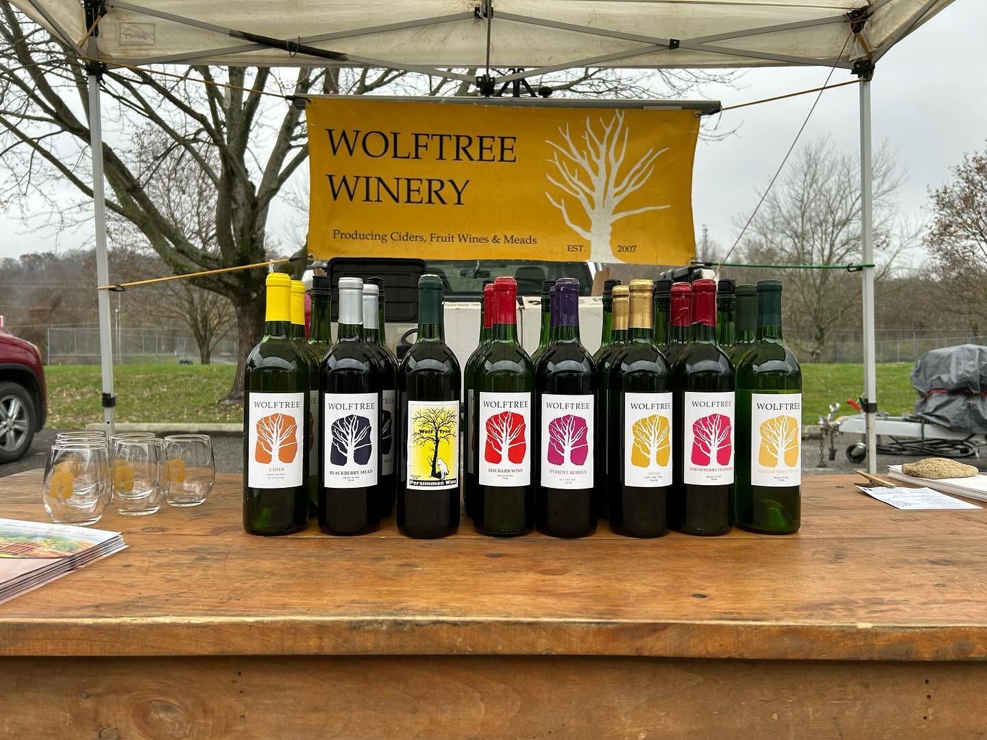 Wolftree Winery wine bottles displayed on a wooden table under a tent at an outdoor market