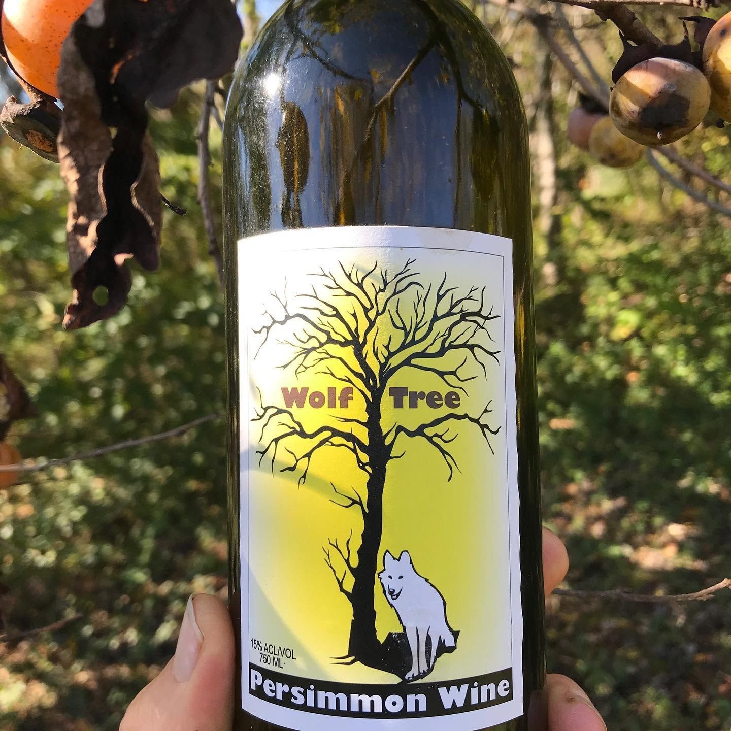 Bottle of Wolf Tree Persimmon Wine with a white label showing a tree and wolf illustration.