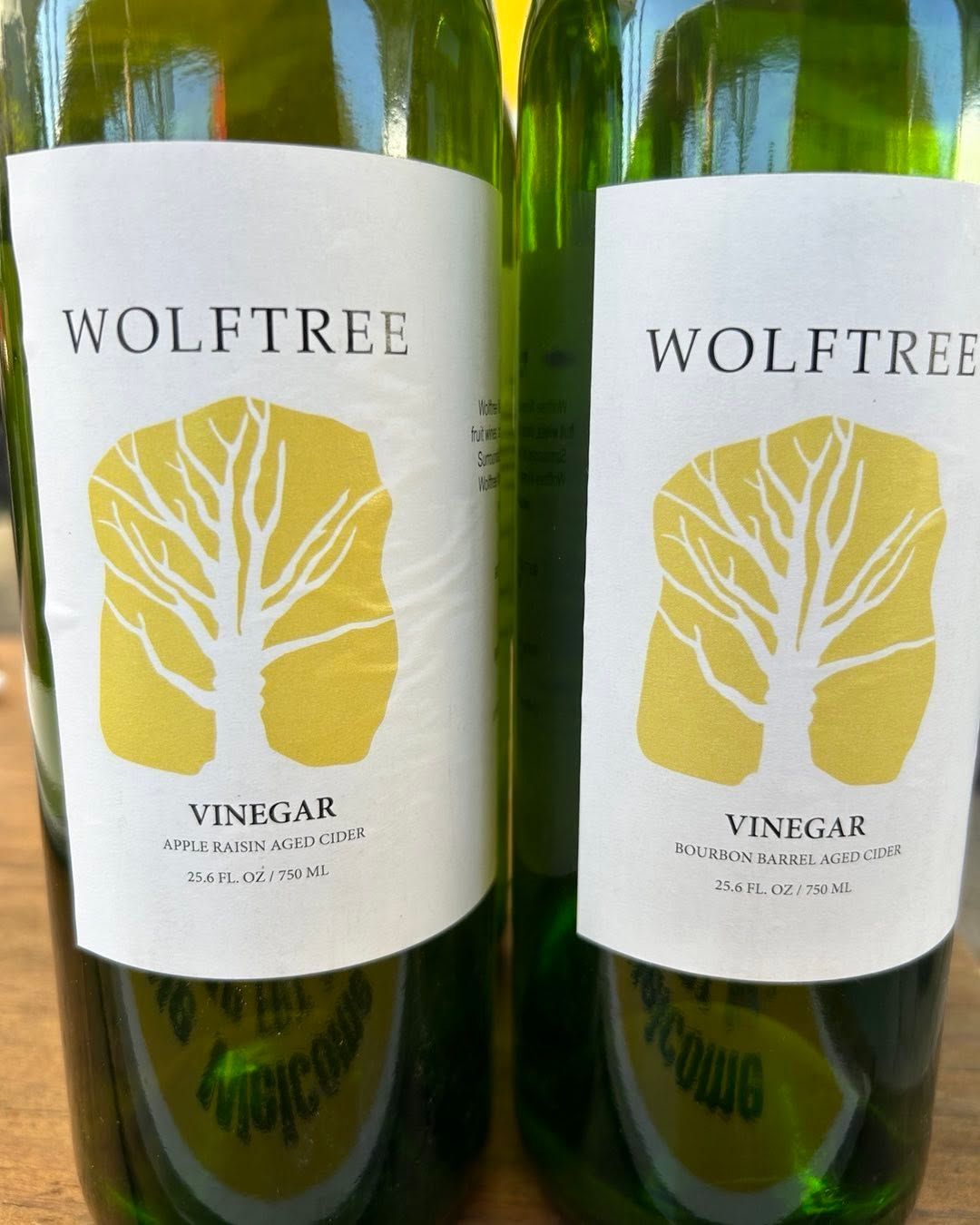 Two WOLFTREE wine bottles with white labels and yellow tree logo against a green background