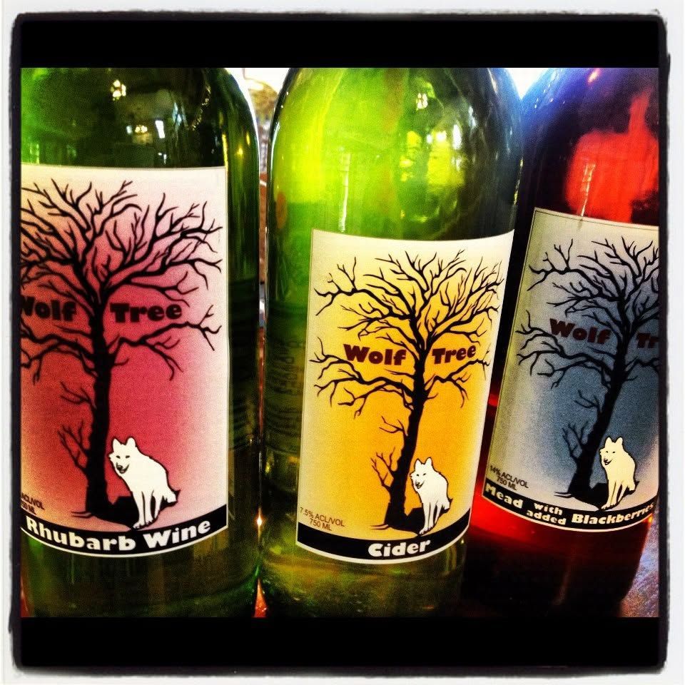 Three Wolf Tree beverage bottles with colorful labels: Rhubarb Wine, Cider, and another red bottle